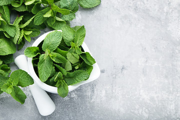 Wall Mural - Fresh mint leafs in mortar on grey wooden table