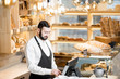 © rh2010 - Handsome bread seller working with cash register in the small and cozy store with bakery products