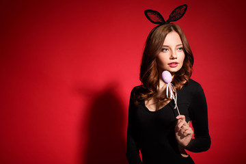 Wall Mural - Young woman studio isolated on red in a rabbit costume holding crafted egg