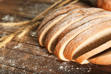 Cut bread and wheat spikes on table