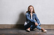 Girl near white wall. fashion hipster teen sits floor.Girl blonde adolescent 11 years.Young caucasian woman model teenager in casual clothes,denim jacket,youth jeans.Concept lifestyle.Copyspace.