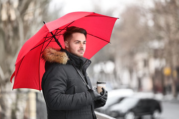 Poster - Young man in warm clothes with red umbrella outdoors