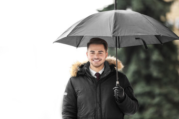 Poster - Young man in warm clothes with dark umbrella outdoors