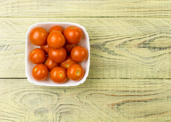 Cherry tomatoes in a white plate on a wooden background.