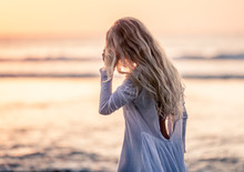 Beautiful Blonde Girl With Long Hair In Short White Dress Walking At Sunset On The Beach In Bali, Indonesia Touching Hair 