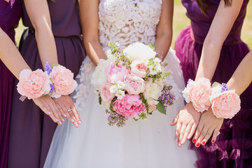 Hands of the bride and girlfriend with decorative flowers in the open air.