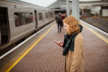 Young Woman Standing On Railway Platform Using Her Mobile Phone
