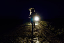 Running Female Silhouette On A Night Country Road Running Away From Pursuers By Car In The Light Of Headlights