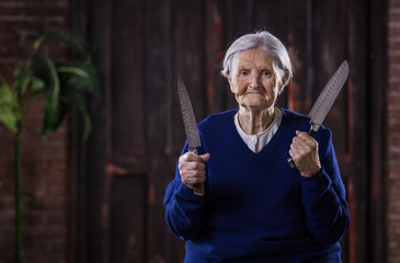 Wall Mural - Senior woman holding kitchen knives indoors. Self defense concept.