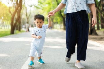 Asian mother walks with her child holding his hand in the spring park. Responsible parenting concept