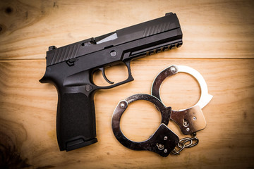 Wall Mural - Hand gun with hand cuffs on wooden surface