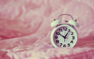 Wall Mural - Vintage alarm clock on pink blanket bed closeup blur background