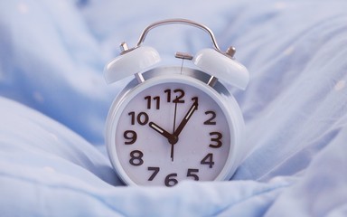 Vintage alarm clock on blue blanket bed closeup blur background