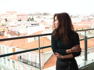 A girl with long hair stand on the roof in front of a panoramic view of the Lisbon and smile