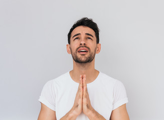 Sticker - Horizontal studio portrait of Caucasian bearded man wearing white T-shirt standing with sad look, keeps palms together, hopes for better and good luck, looks up for praying.Human expressions, emotions