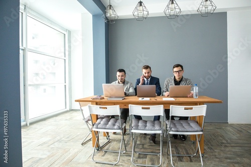Photographie Three businessmen working at laptops sitting at the table