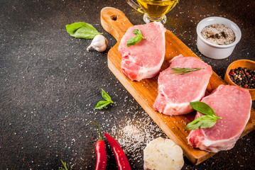 Wall Mural - Raw meat, pork steaks with spices, herbs, olive oil, dark background  copy space