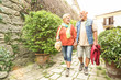 Happy senior couple walking holding hand in San Marino old town castle - Active elderly and travel lifestyle concept with retired mature people at Italy roadtrip - Sunshine halo with sunflare filter