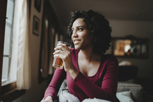 Woman Having Drink While Looking Through Window At Home