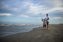 Playful Father And Sons With Fishing Rod Standing At Beach 