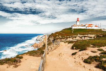 Beautiful seascape. View from the cape of rock to the lighthouse over the Atlantic Ocean and two people standing in the distance on the cliff, Portugal. Sintra. Cape of rock.