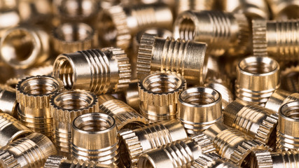 Bronze threaded inserts as background. Close-up of decorative pile from golden metal parts. Idea of construction, build, store or mechanical engineering. Great depth of field.