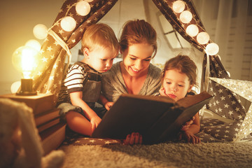 Wall Mural - happy family mother and children reading a book  in  tent at home.