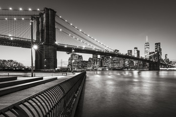 Fototapete - Brooklyn Bridge Park boardwalk in evening with the skyscrapers of Lower Manhattan, East River, and the Brooklyn Bridge in Black & White. Brooklyn, New York City