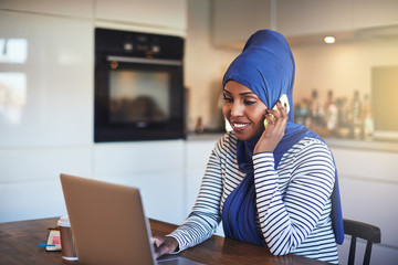 Wall Mural - Smiling Arabic entrepreneur talking on a phone in her kitchen