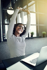 Wall Mural - Young African woman smiling and stretching while using a laptop