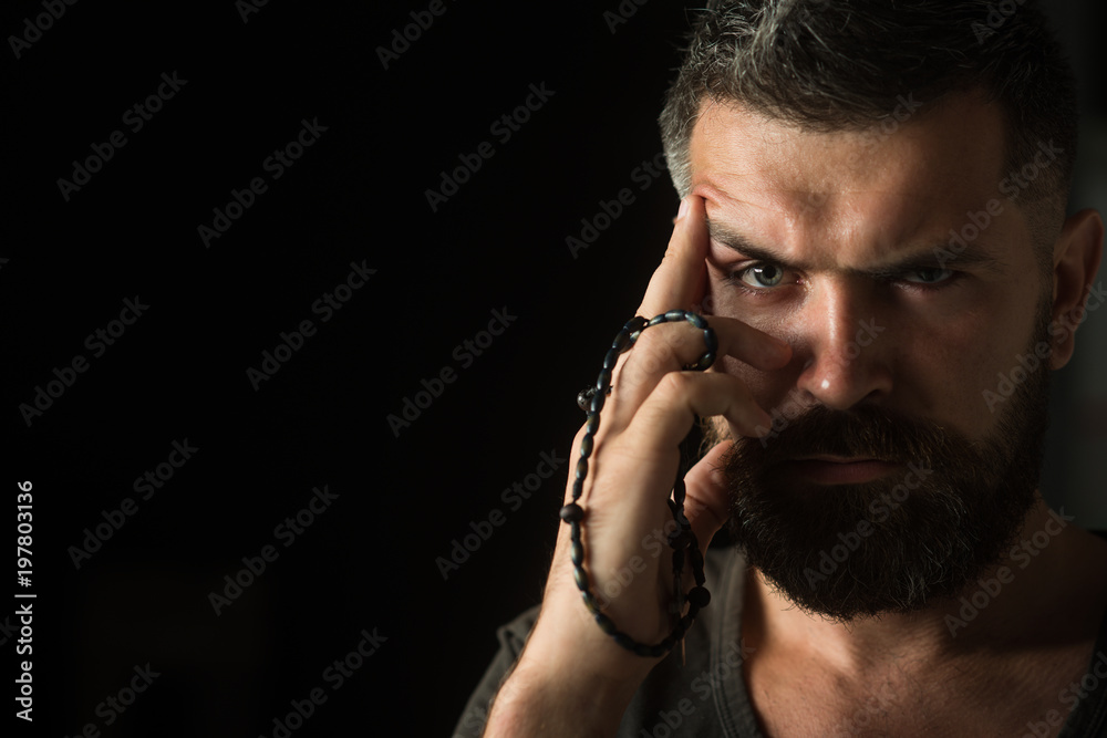 Handsome bearded man with stylish hairstyle with rosary beads in hand