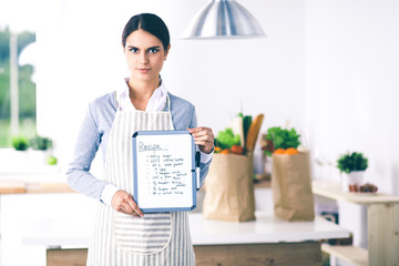 Woman in the kitchen at home, standing near desk with folder