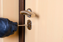 A Man's Hand In A Black Leather Glove Holds The Key. Keyhole In The Door.