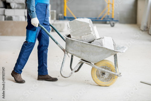 Fotografía Builder carrying blocks on a wheelbarrow at the construction site indoors