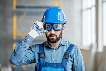 Close-up portrait of a handsome bearded builder with protective glasses and helmet indoors