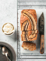 Butter-free, sugar-free banana bread with oat flour, soft curd cheese and honey. Top view of sliced banana bread on gray cement background. Ideas and recipes for healthy diet breakfast. Vertical.