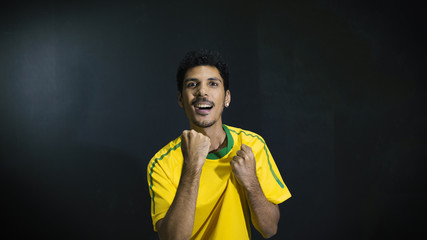 Wall Mural - Male athlete or fan in yellow uniform celebrating on black background