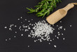 Salt heap on black background with rosemary herb and wooden spoon