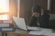 © thithawat - attractive business woman working bend down the head with tired on table with laptop and coffee cup in office dark tone.