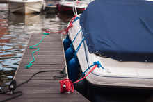 A Modern Motor Boat Windshield And Bow Deck Covered In A Blue Canvas Rain Cover, With A Weathered Wood Dock And Blurry Port In Background