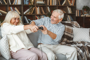 Wall Mural - Senior couple together at home retirement concept sitting playing man taking away controller