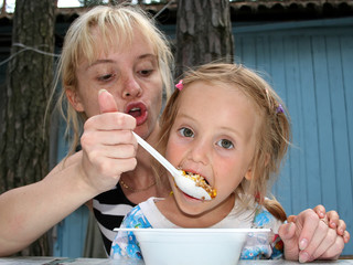 Mom is feeding a little daughter from the spoon outdoors