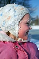 A laughing little girl with cheeks red from frost and with a snow on her face and hat