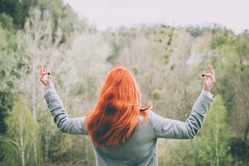 Redhead girl meditating on the edge of the hill in front of the green forest mountain. Concept idea of meditation, calmness, travel, consciousness, dreaming, harmony.