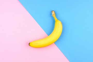 Single yellow banana over a pink and blue background. Top view, minimal concept.