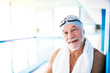 © Halfpoint - Senior man standing by an indoor swimming pool.