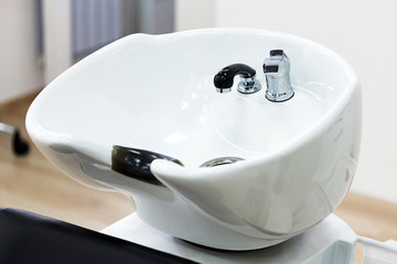 Closeup shot of chair with bowl for hair washing in hairdresser salon. Main focus is on the faucet