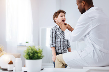 Wall Mural - Little patient. Appealing charming boy catching cold while showing throat to doctor and opening mouth