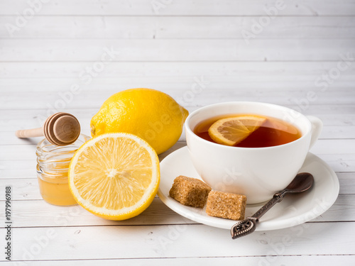 Herbal black tea in a white Cup, honey in a jar of fresh lemon on white wooden b Poster