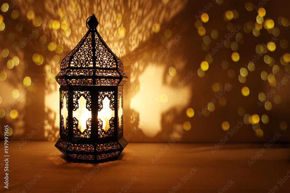 Ornamental Arabic lantern with burning candle glowing at night and glittering golden bokeh lights. Festive greeting card, invitation for Muslim holy month Ramadan Kareem. Dark background. - obrazy, fototapety, plakaty 